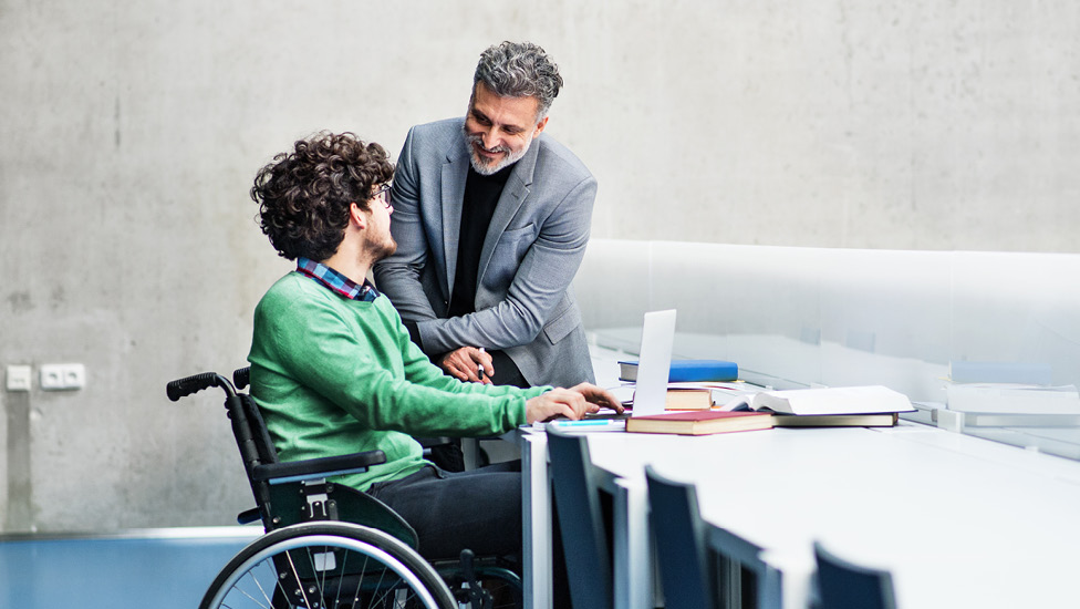 A professor is smiling and chatting with a student in a wheelchair