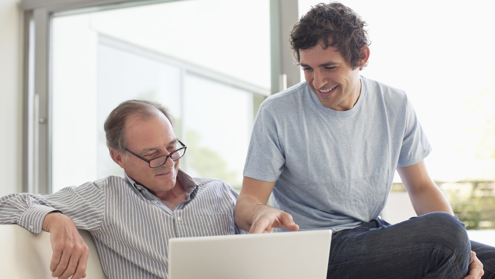 Father and son talking on couch working on computer