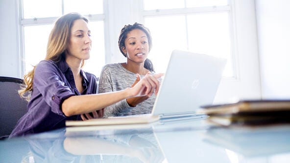 Two women at a table working on a computer. 