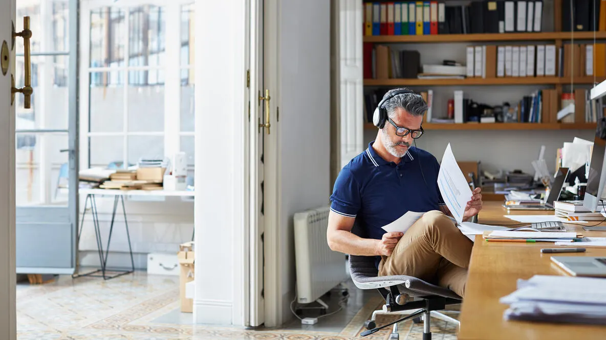 Man wearing headphones looking through paperwork in home office.