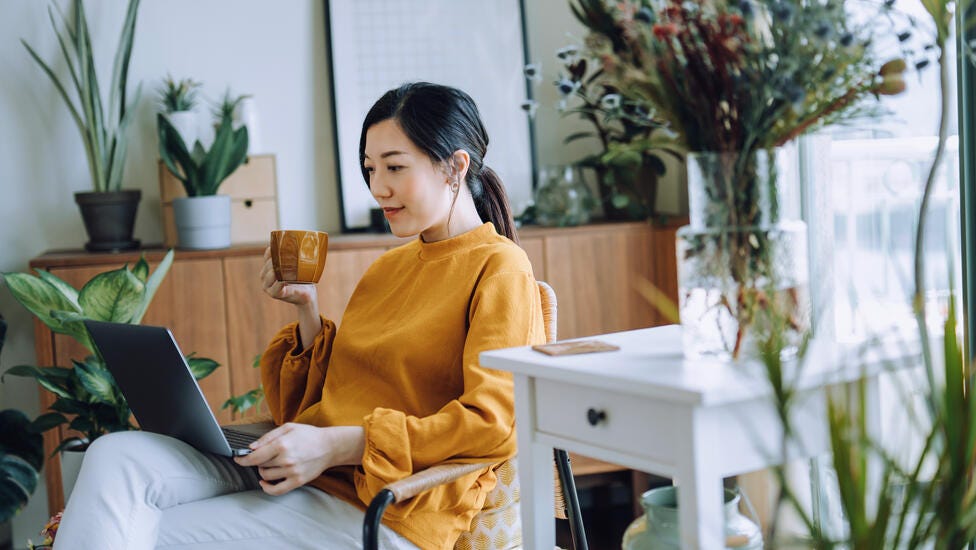 A women reading on her computer while enjoying a cup of coffee.