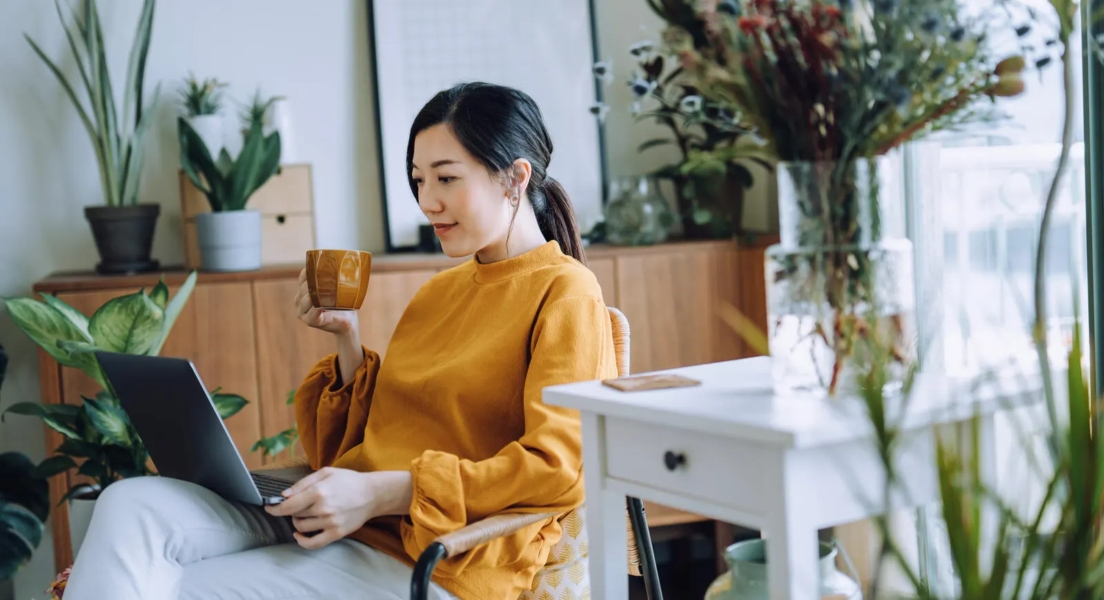 A woman sitting and drinking from a mug, with her laptop on her lap