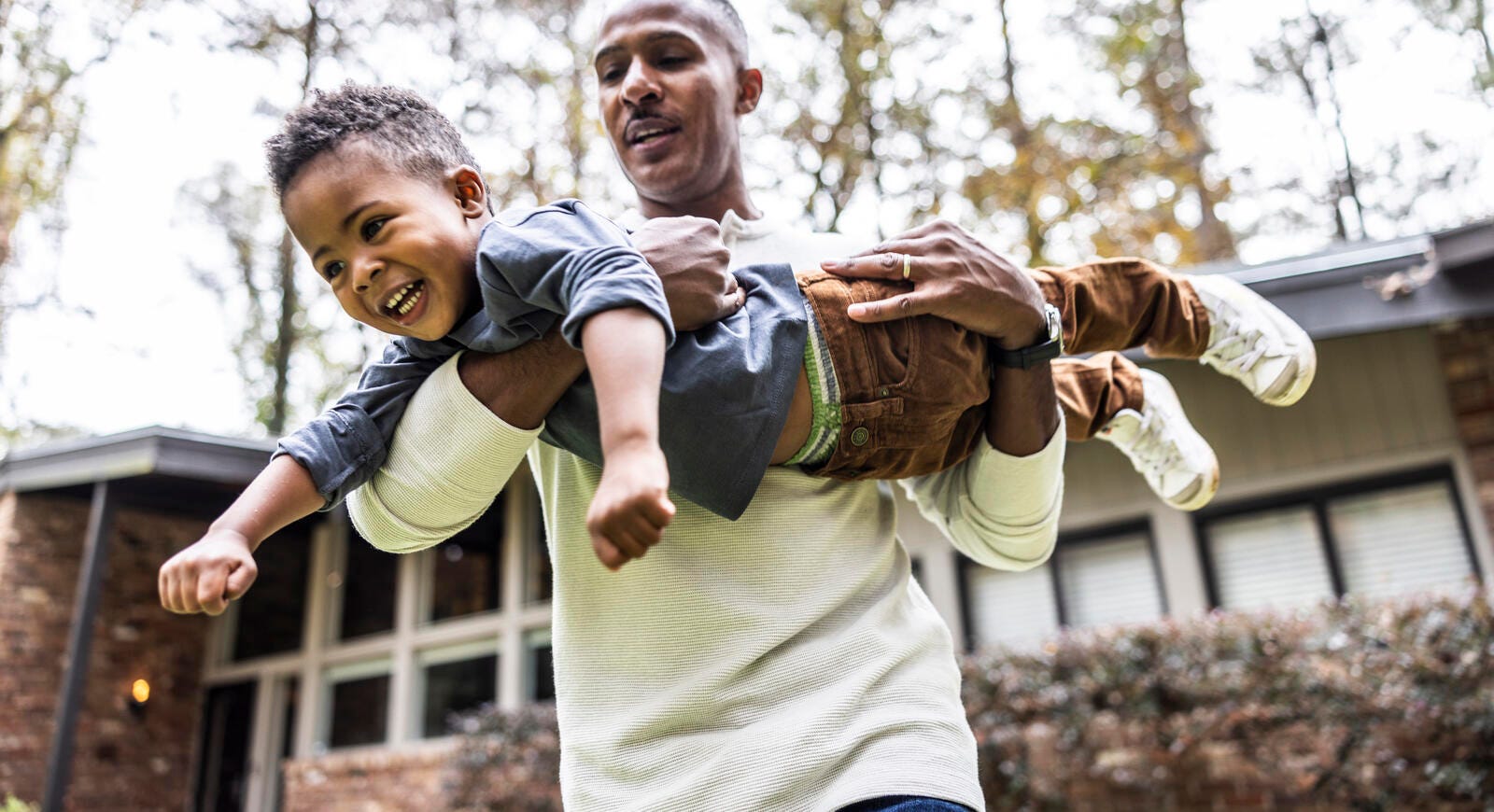 A child pretending to fly in his father's arms.