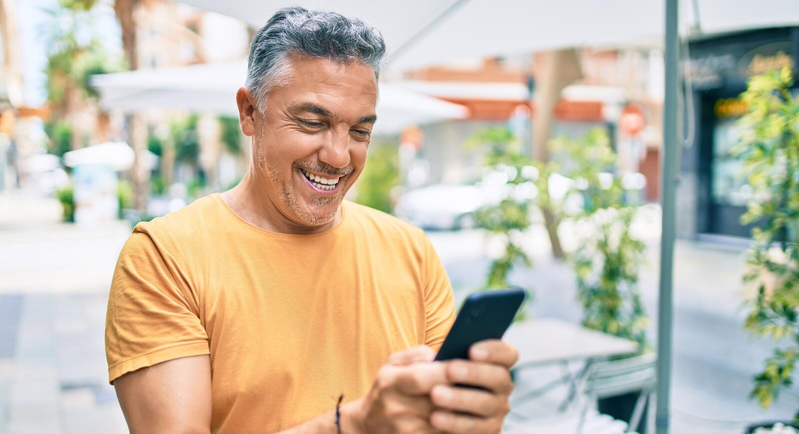 Adulto mayor sonriendo mientras mira un celular en una cocina.