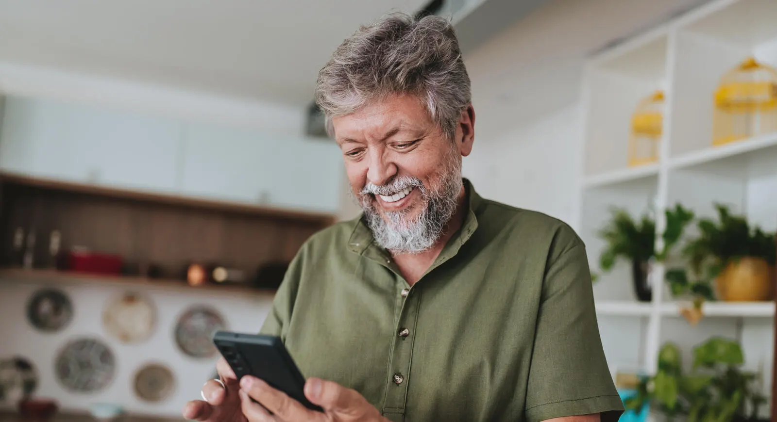 Hombre de mediana edad sonriente mirando su celular en un café al aire libre.