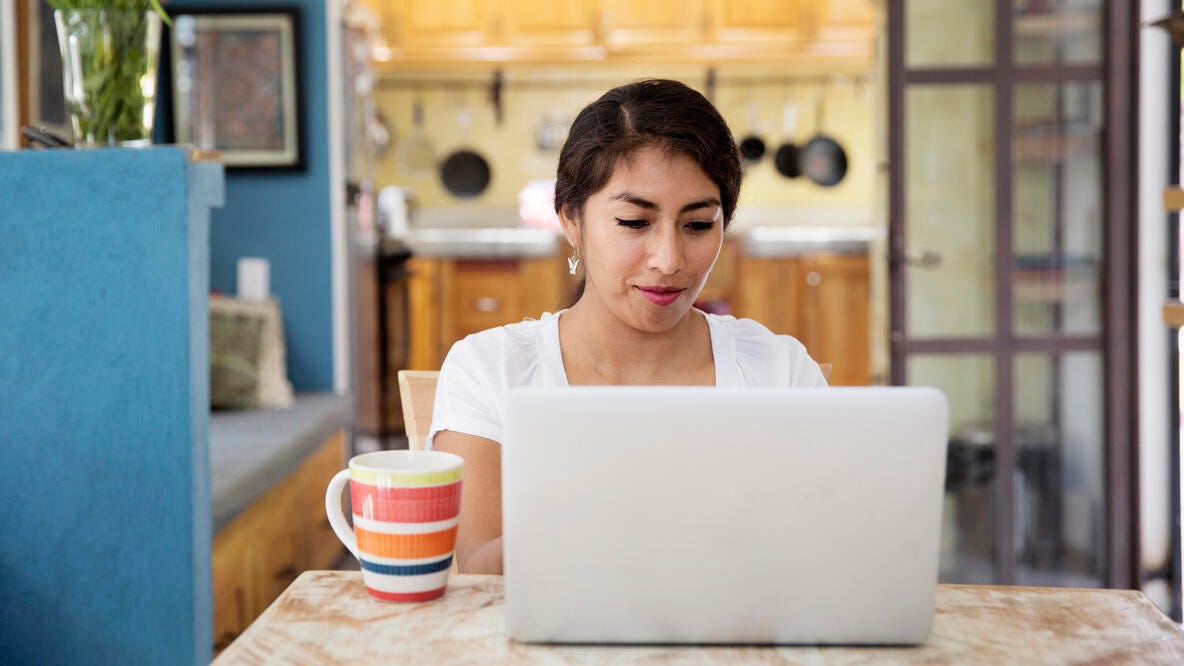 Mujer de mediana edad usando una laptop en el comedor.