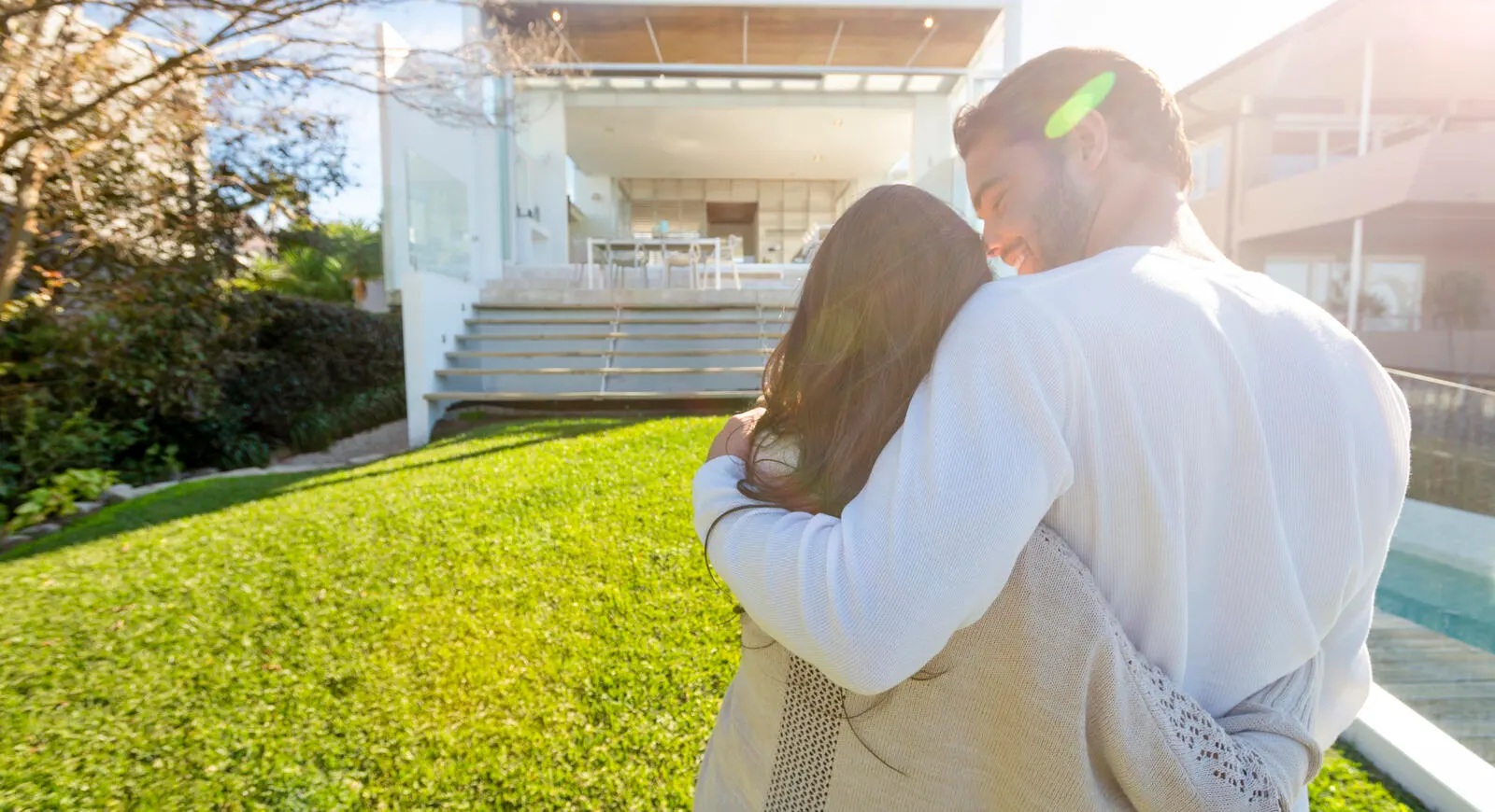 Couple with arms around each other in the back yard looking at a house.