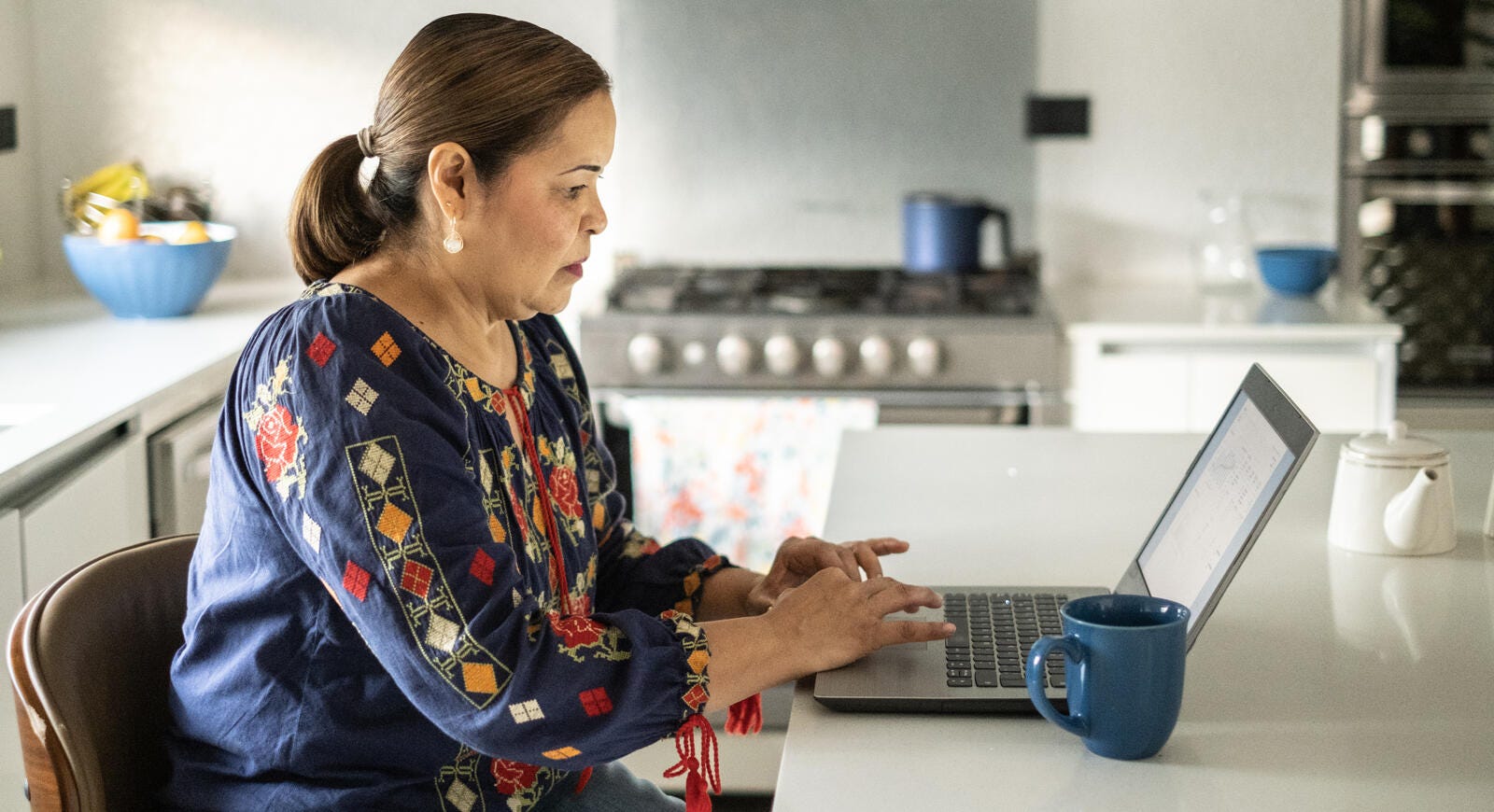 Mujer mayor usando una laptop en la cocina.