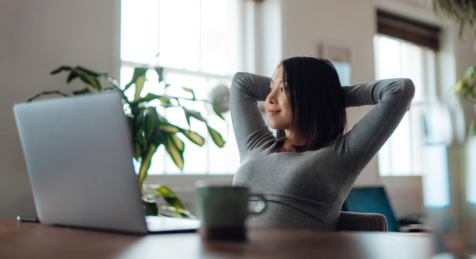 A woman leaning back in a chair with a mug and laptop in front of her