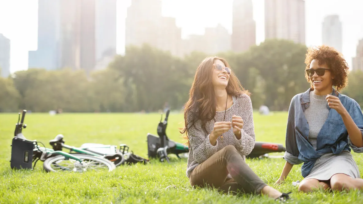 Happy friends talking while sitting on the grass in NYC park