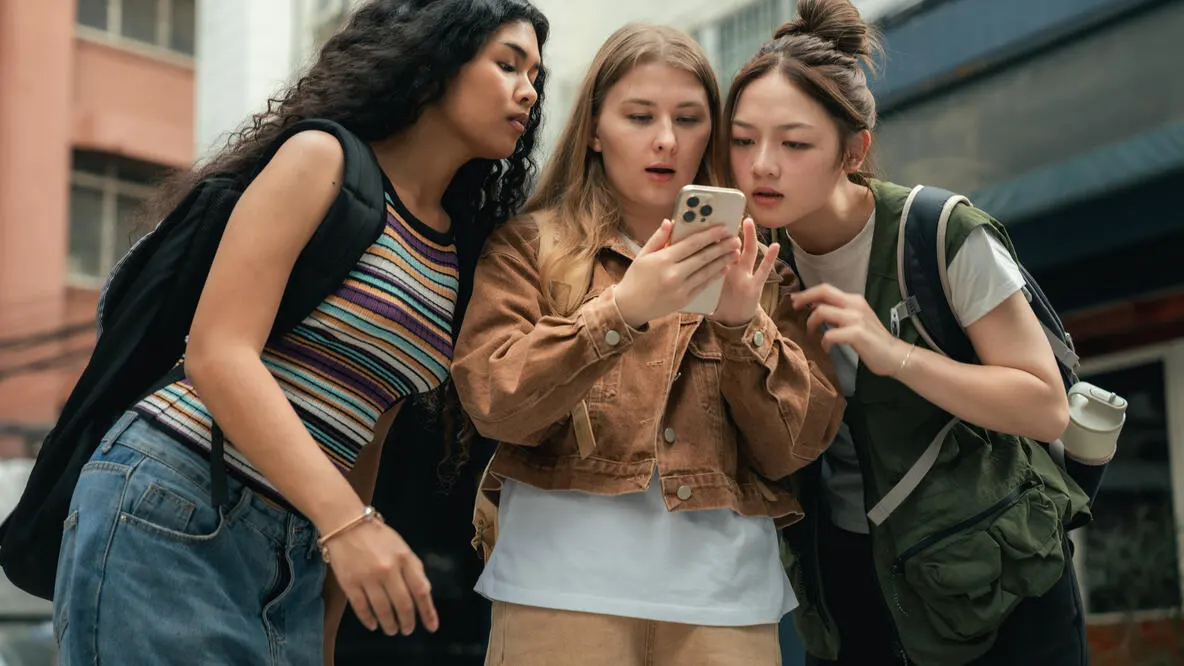Three girls huddled together looking at a smart phone.