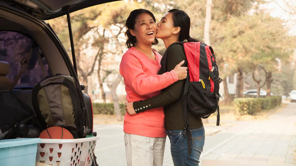 Mother and daughter embracing behind car on college campus