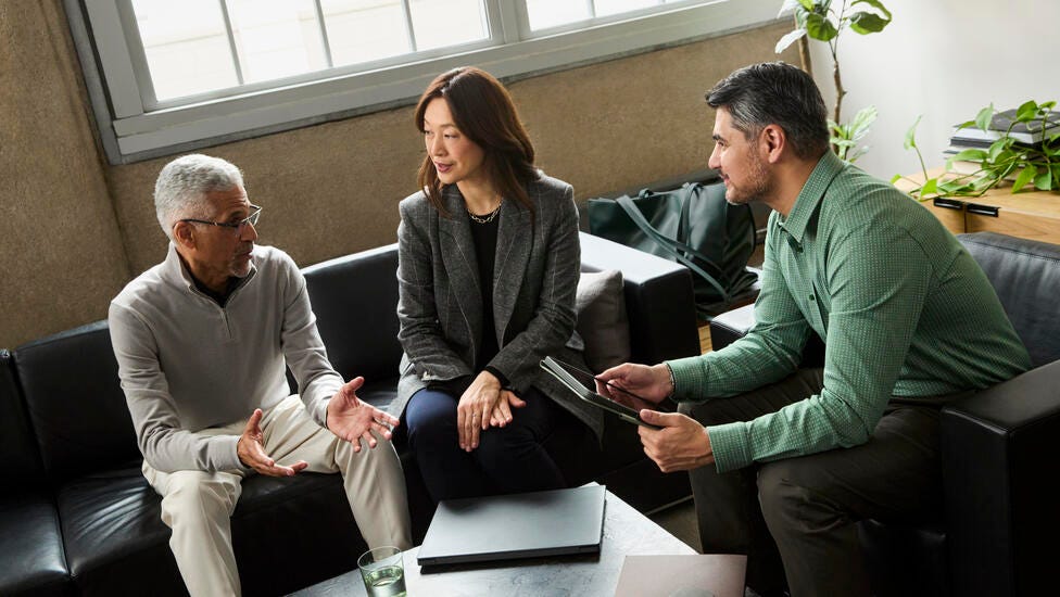 Three people sitting on black couches talking to each other