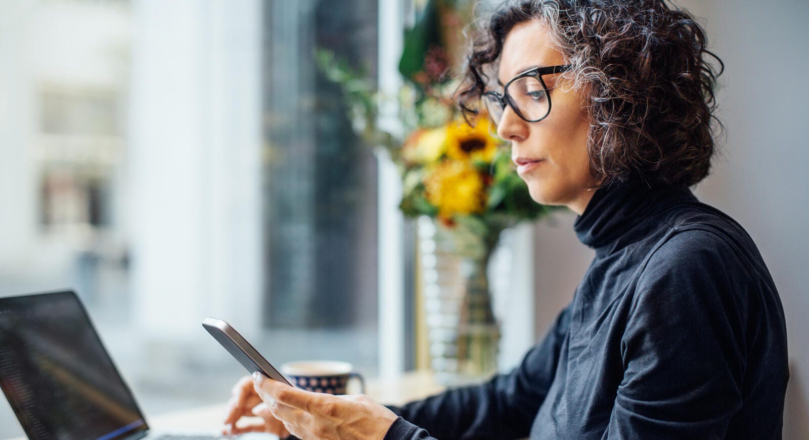 Mujer de mediana edad usando una laptop y un teléfono celular