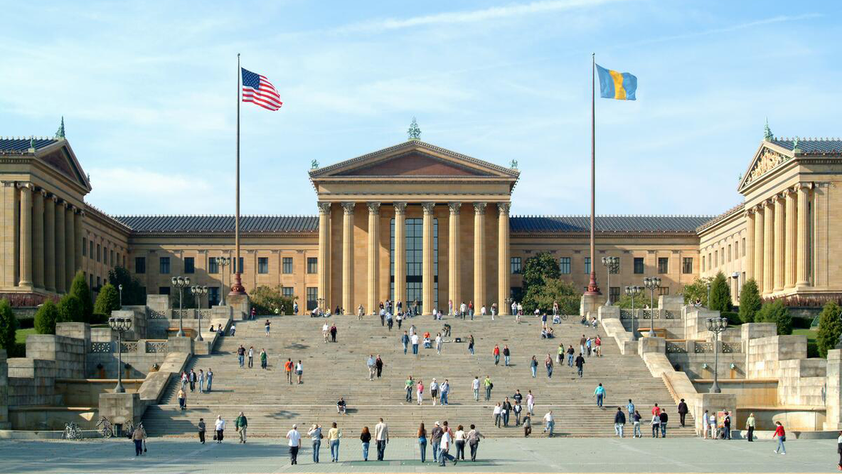 A distant shot of people walking up and down the stairs in front of the Philadelphia Museum of Art.