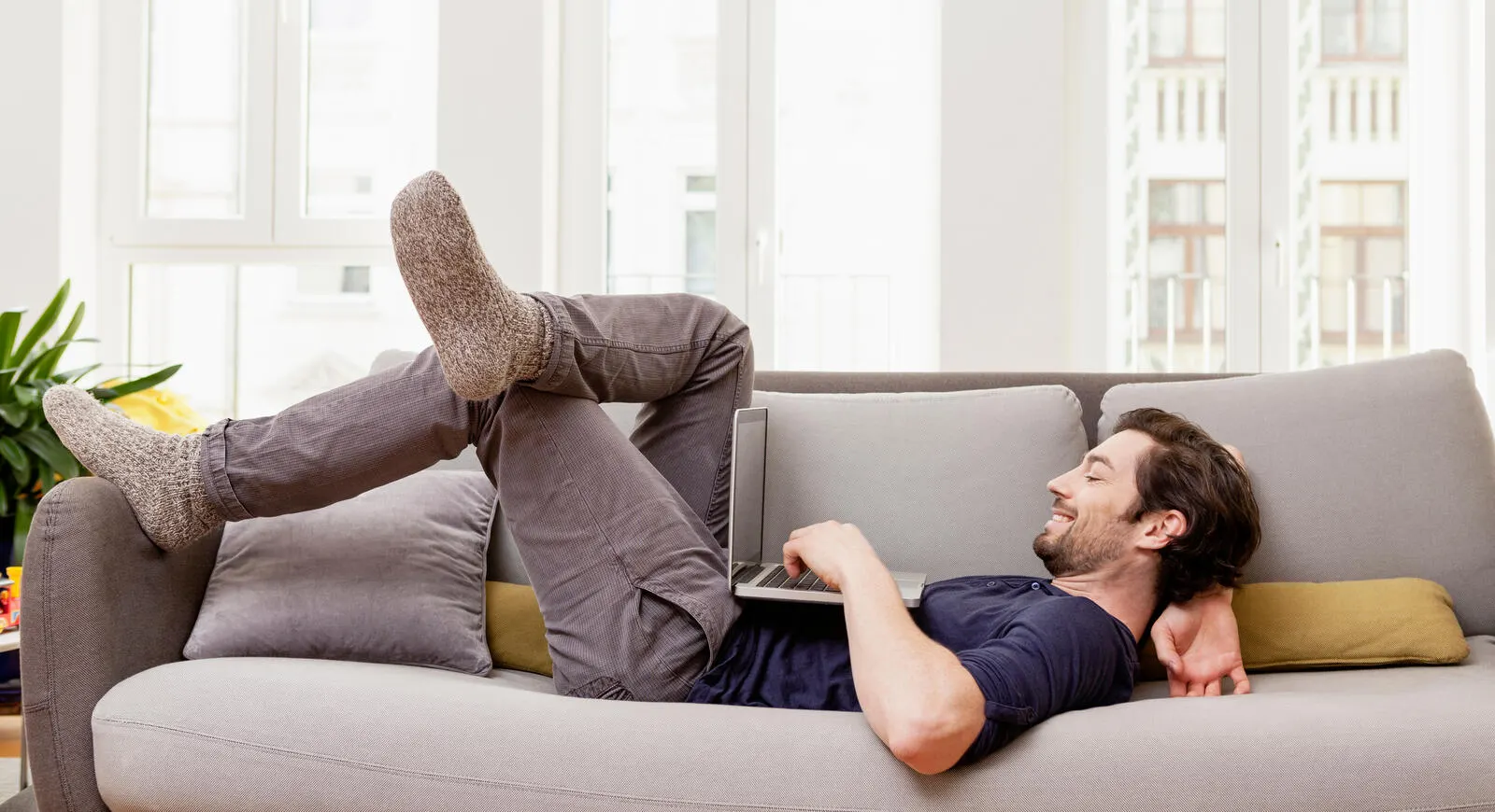 A young man laying on the couch while using his laptop.