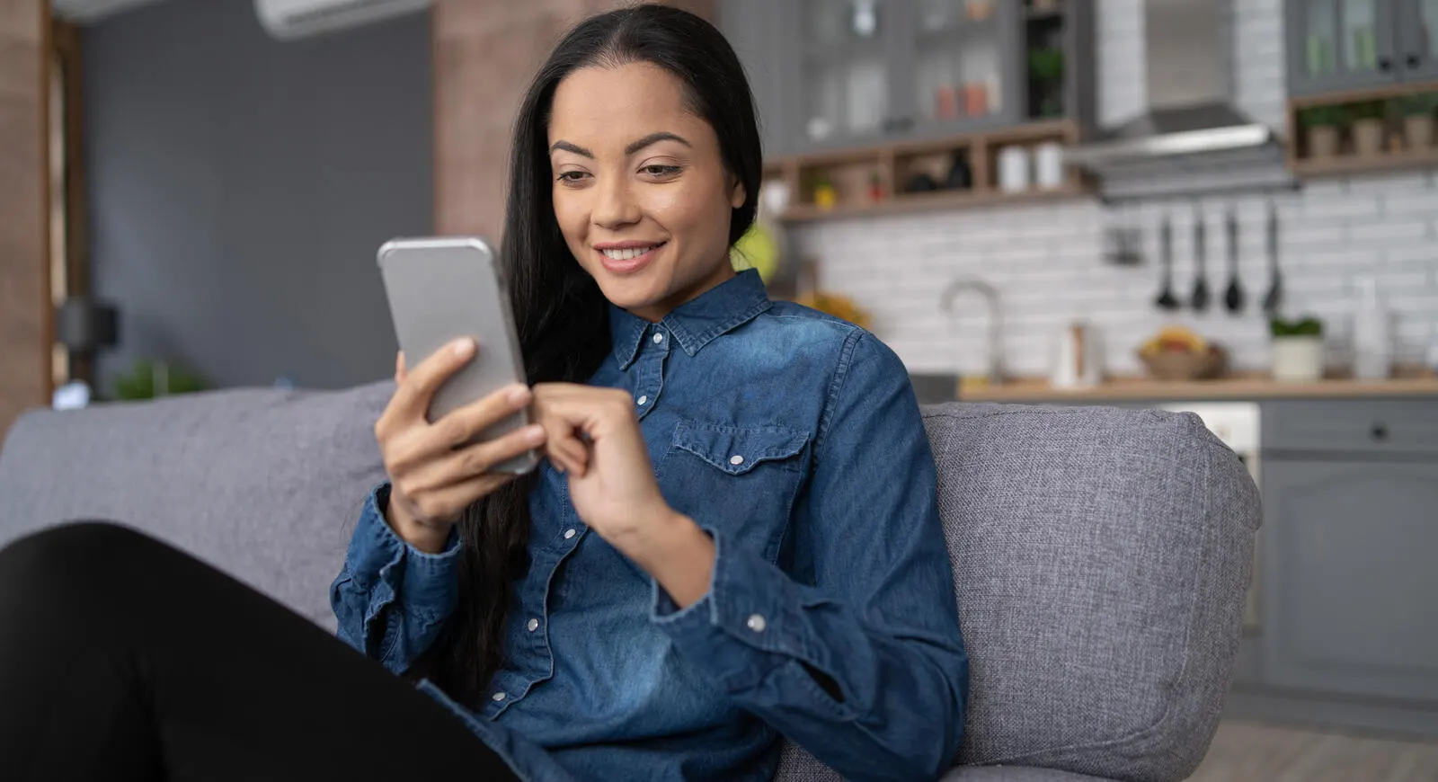 A women relaxing on the couch while doing her banking on her phone.