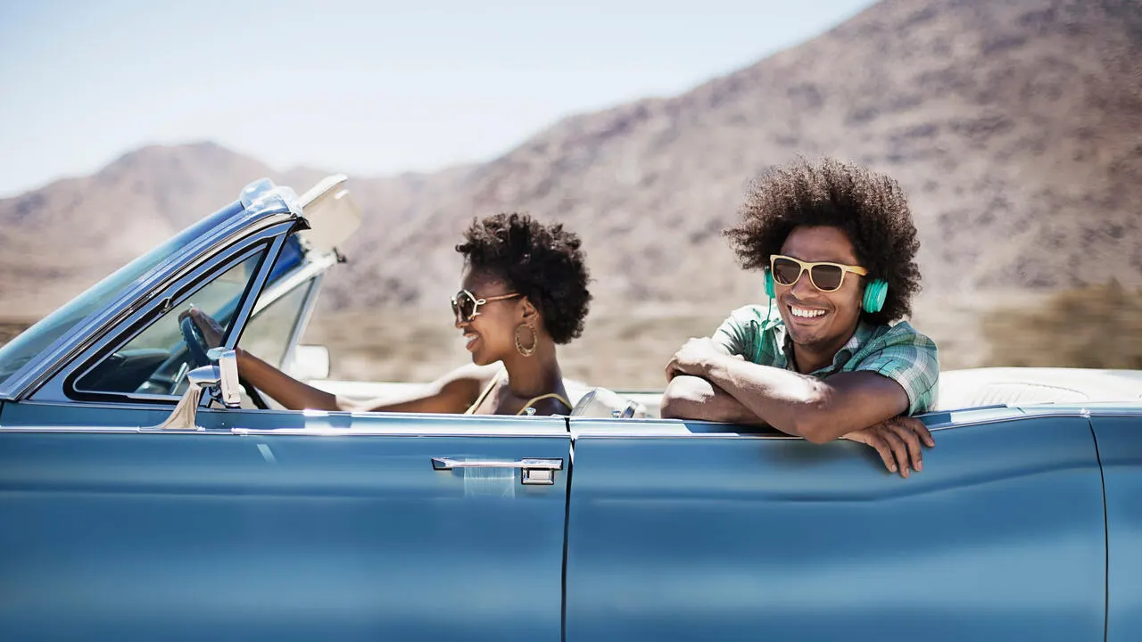 A young couple in a pale blue convertible on the open road, with the top down. 