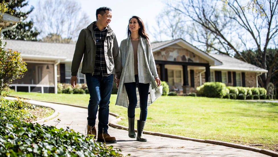 A couple holding hands while walking down their long driveway.