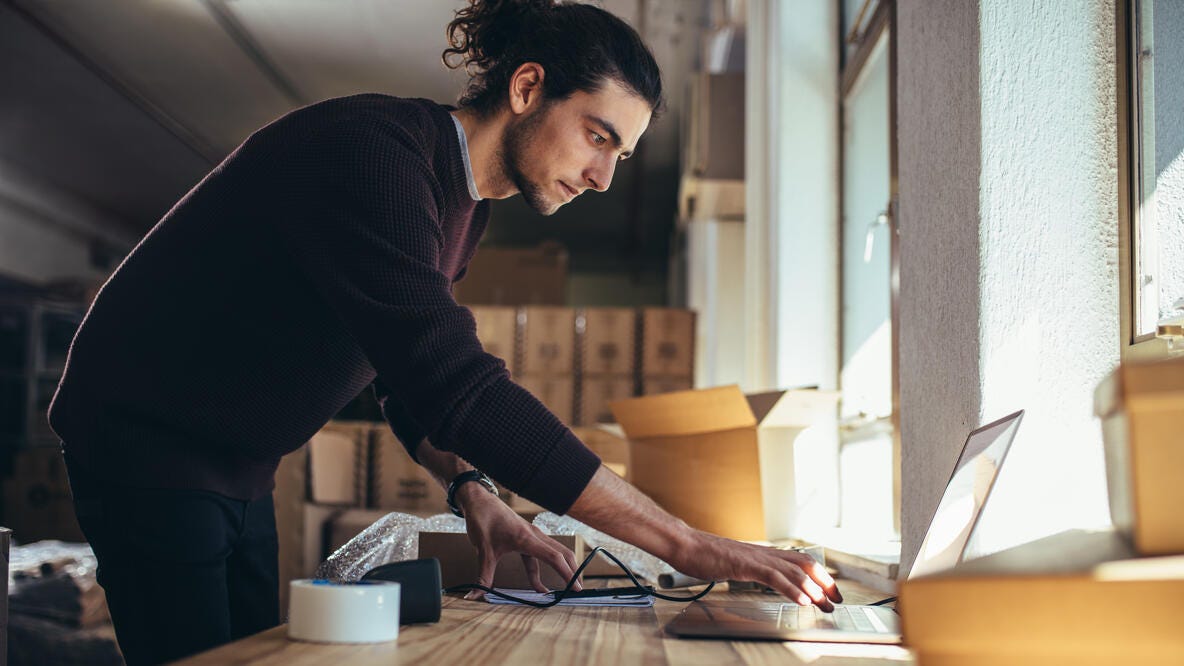 A small business owner using a computer while preparing to ship some orders.