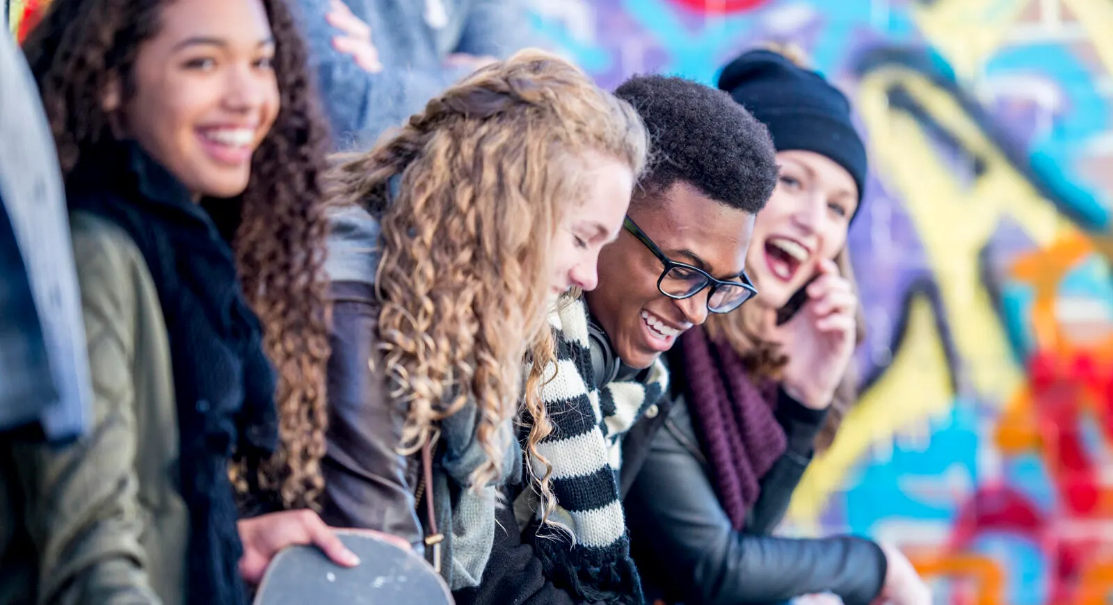 A group of teenagers are sitting outdoors in front of graffiti wall