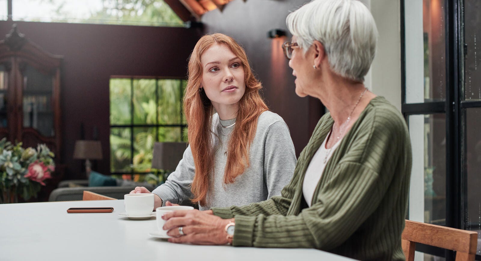 young woman having coffee with her elderly mother at home
