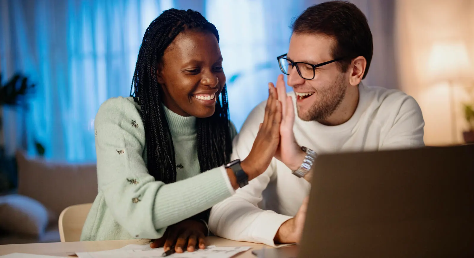 Man and woman sitting at a computer giving each other a high-five while smiling.