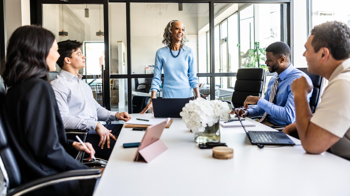 A woman stading at a conference table talking to her team in a meeting room.