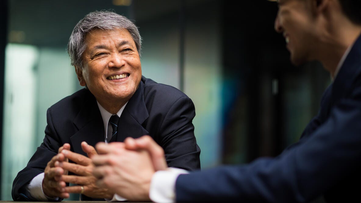 Two men sitting in a conference room smiling.