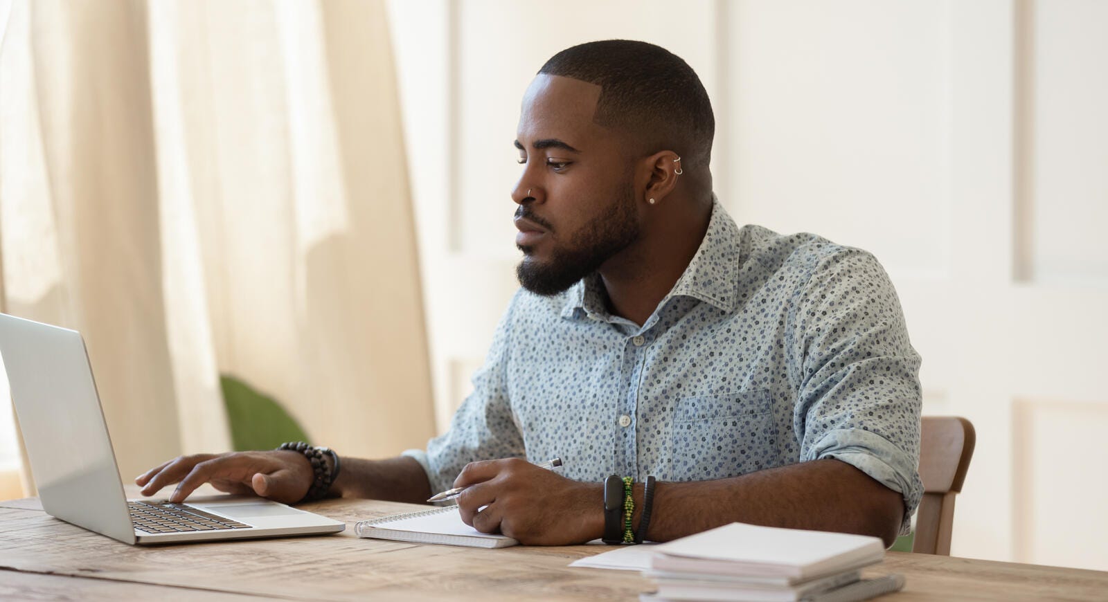 man sitting at a table using a computer and taking notes
