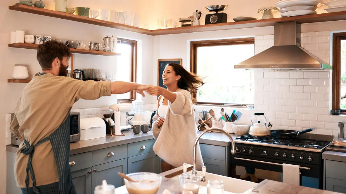 A man and a woman dancing in the kitchen while cooking.