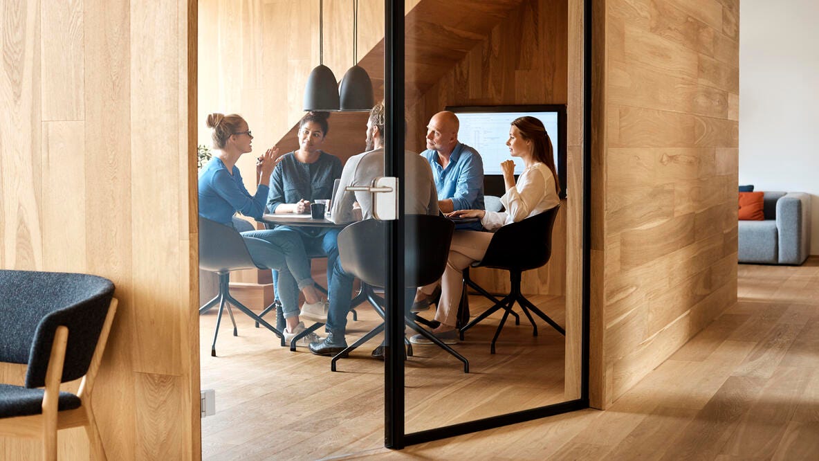 A small group of coworkers meeting in a modern wood and glass meeting room.