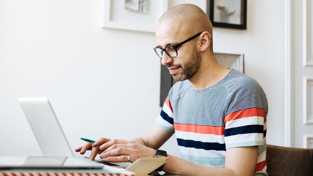A man with a striped shirt and glasses working on his computer.