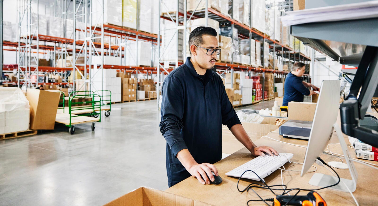 A male warehouse worker checking orders at a computer work station.