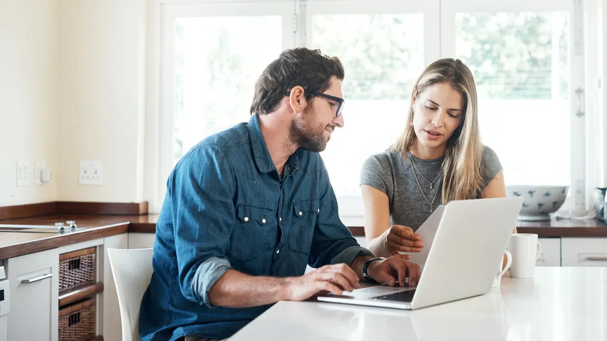 A couple looking at paperwork while using their laptop.