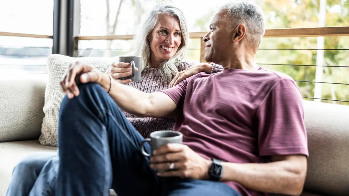 A couple smiling on the couch while having coffee.