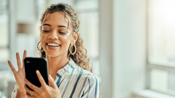 A woman smiling while using her smartphone.